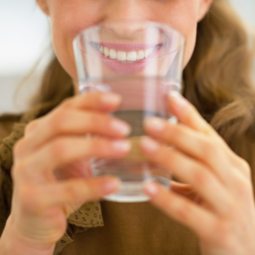 A woman smiles as she brings a glass of water to her lips.